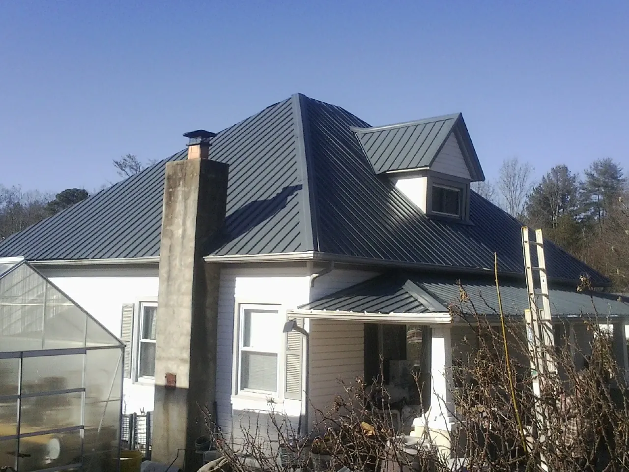 Dark blue standing seam metal roof on a white farmhouse with dormer — Slate & Tile Roof Repair by Roofing Brothers in Stittville