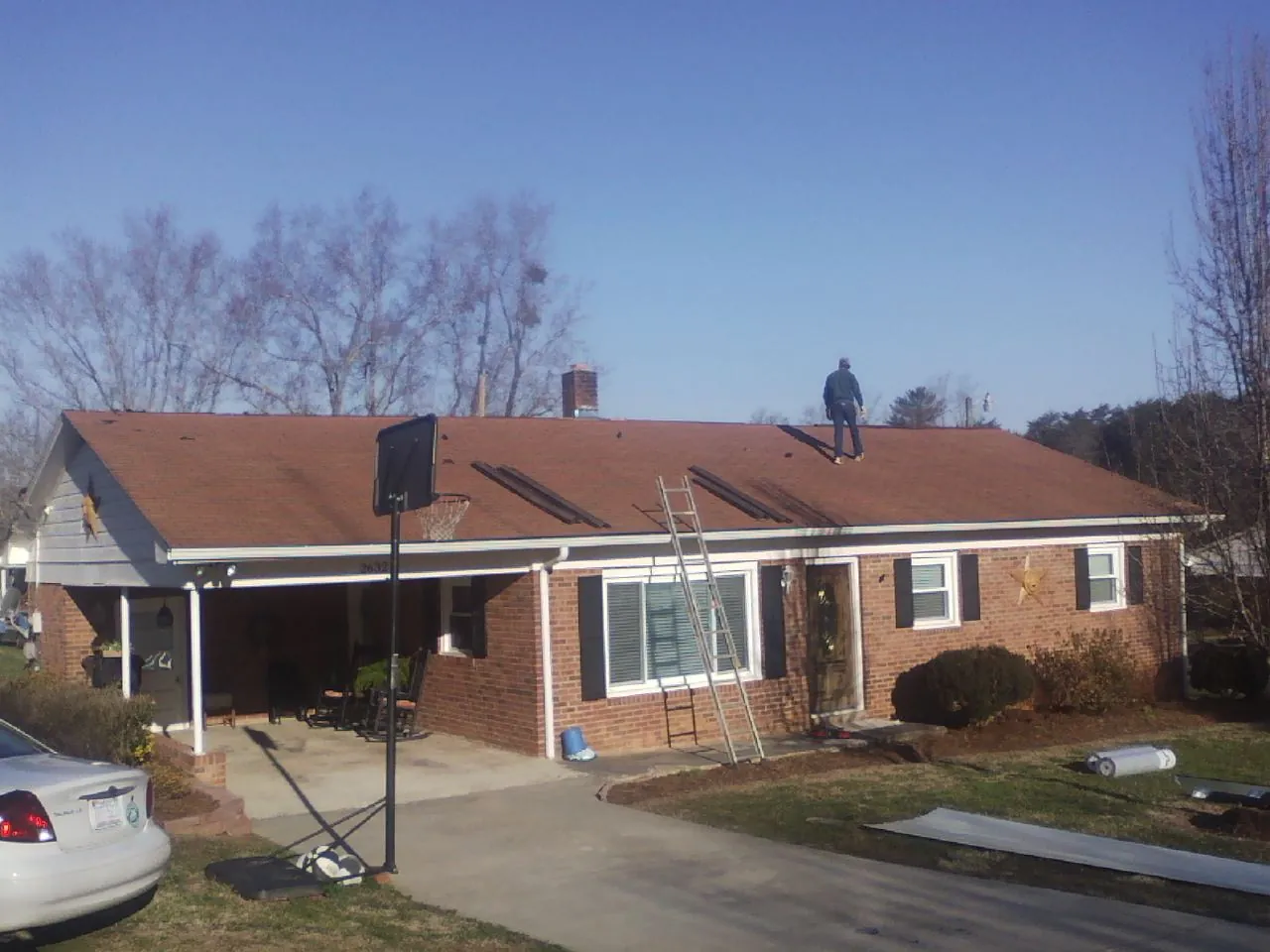 Roofer stripping a shingle roof on a brick ranch before metal panels in Stittville
