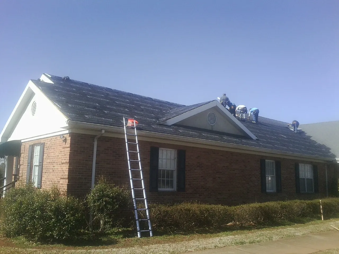 Crew tearing shingles off a brick ranch roof with a ladder set — Emergency Roof Repair work by our crew in Stittville