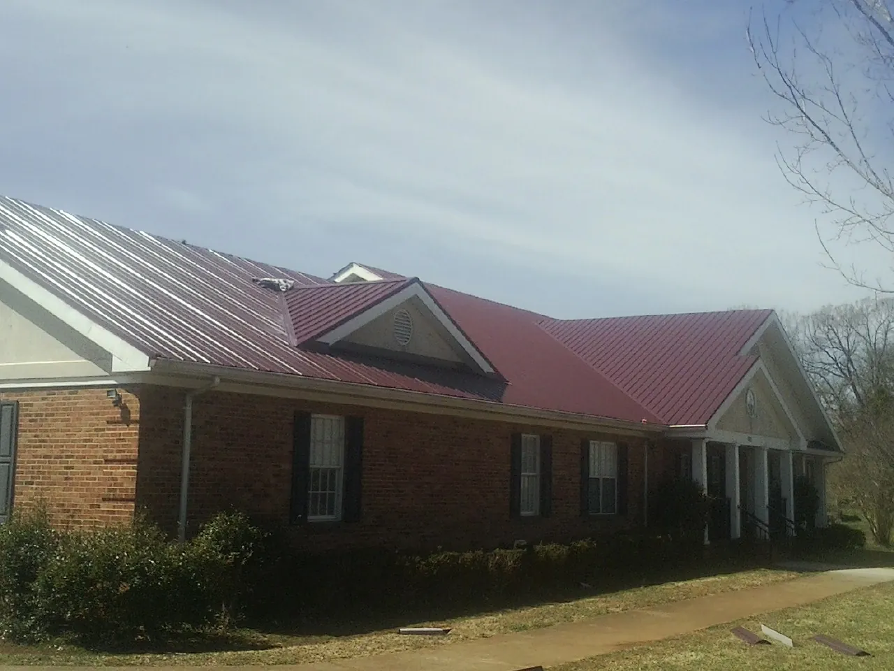 Red metal roof with gabled entries on a long brick building, from a Hail Damage Roof Repair job in Stittville