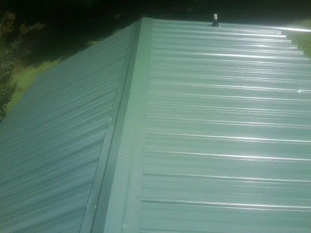 New green metal panels meeting at the ridge of a roof — Flat Roof Repair work by our crew in Stittville