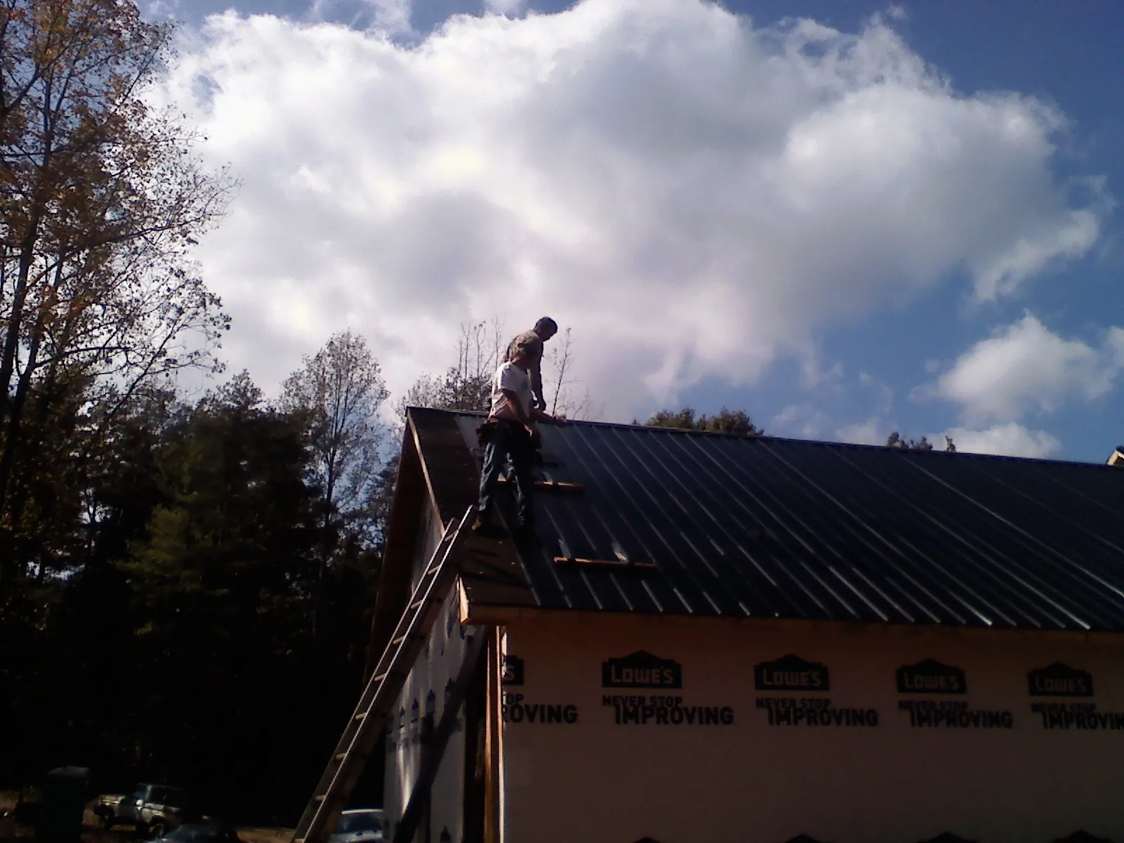 Roofer fastening dark metal panels high against a cloudy sky, from a Roof Inspection job in Stittville