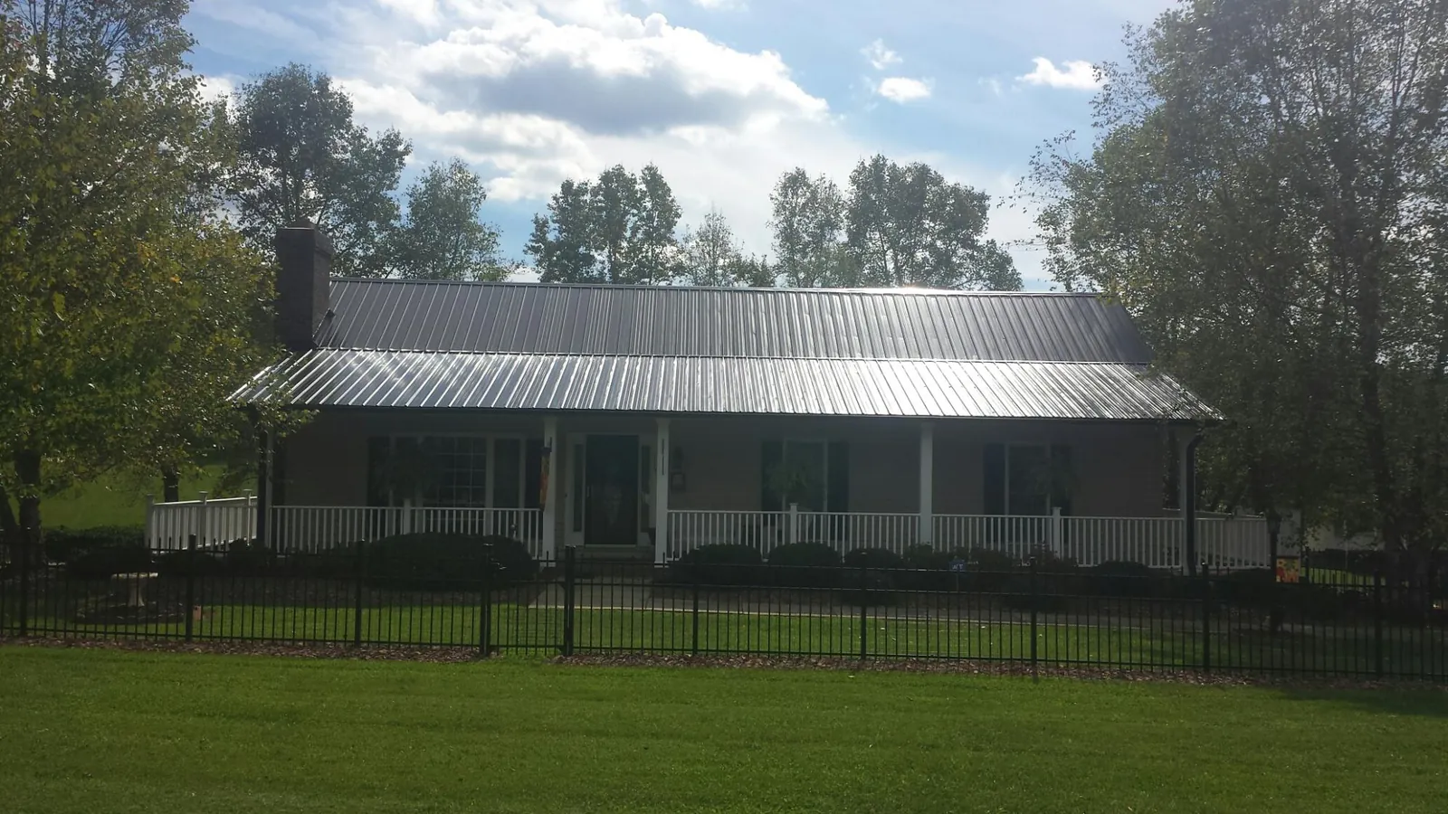 Gray metal roof on a brick ranch with a full width front porch — Gutter Guard Installation work by our crew in Stittville