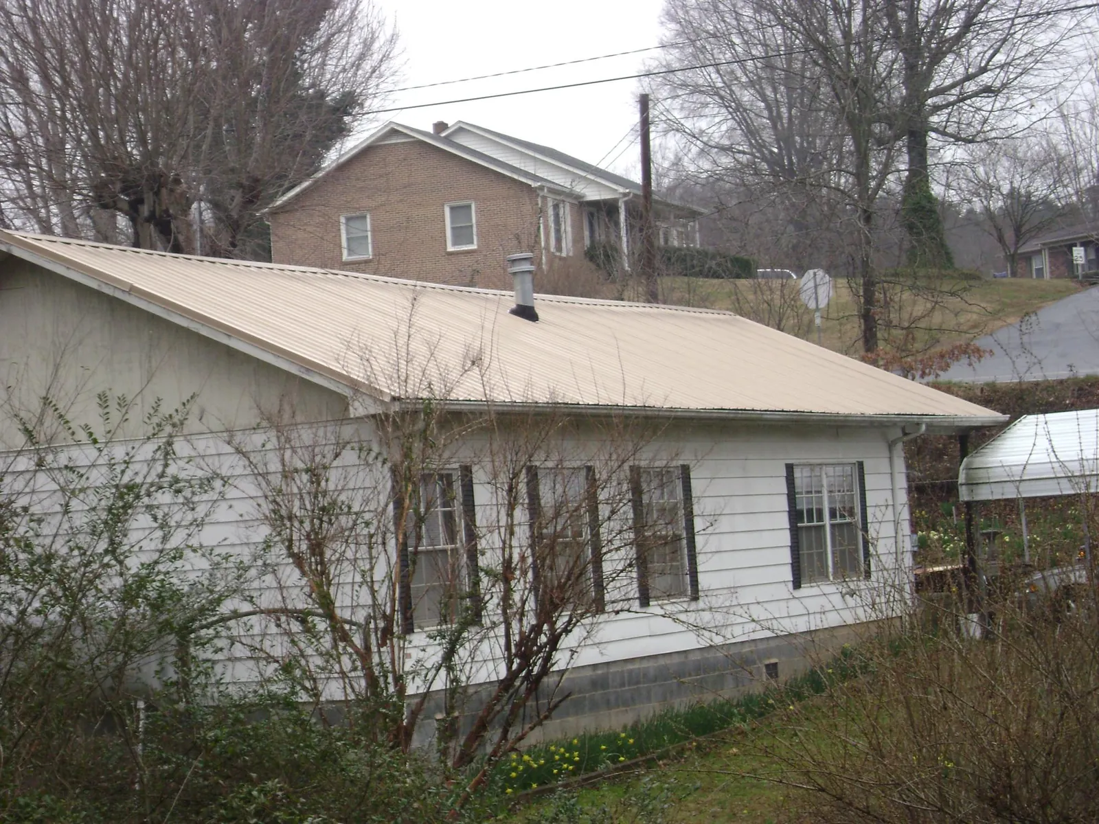 Tan metal roof on a white sided house set into a hillside — Commercial Roofing by Roofing Brothers in Stittville